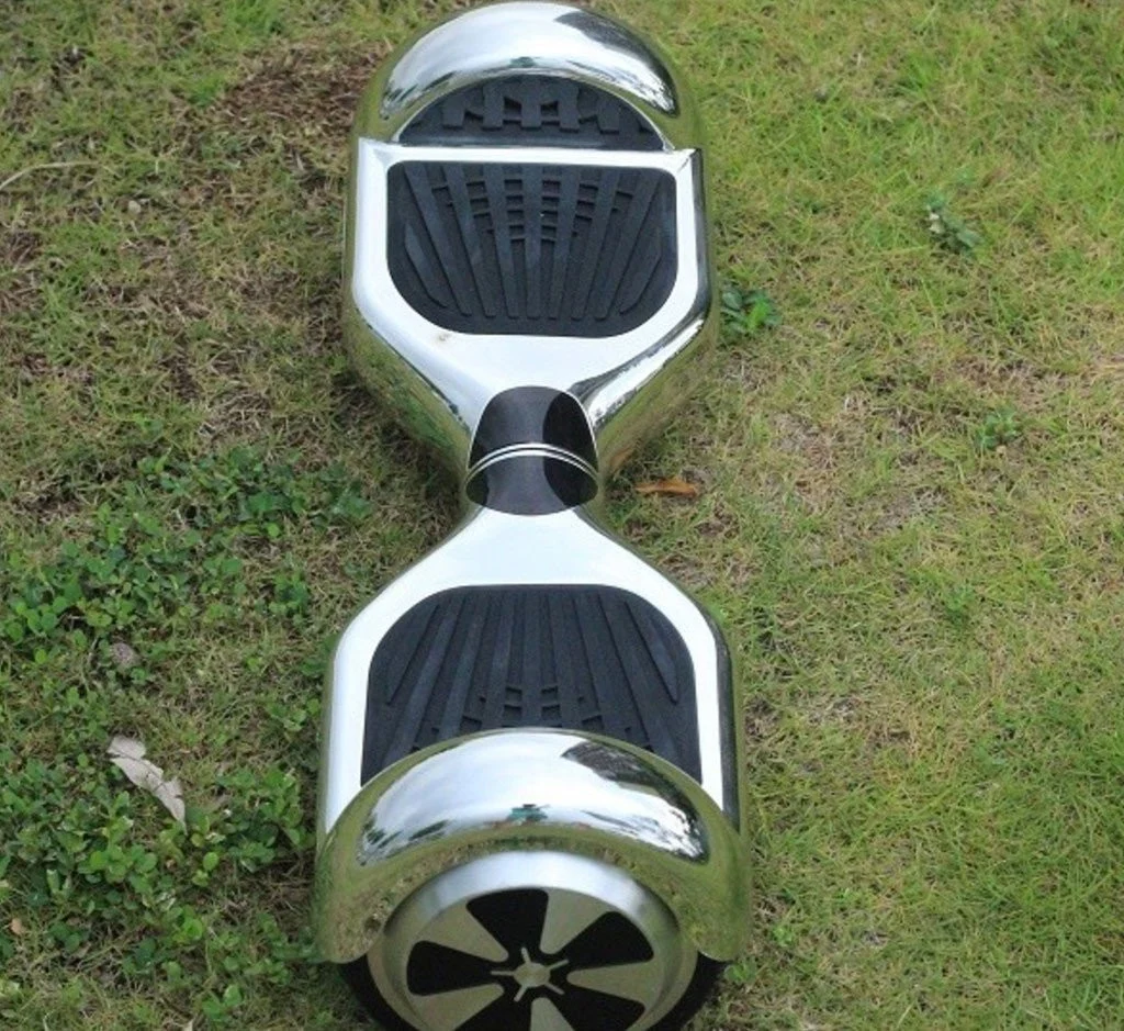 Chrome silver self-balancing hoverboard resting on green grass outdoors, calm daylight mood